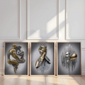 Gold-framed three-piece abstract couple art leaning against white paneled wall in sunlight