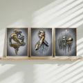 Three gold-framed gold-and-silver figurative prints displayed on slim wood shelf