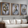 Three gold-framed surreal gold-and-silver figure prints above white sofa on gray paneled wall