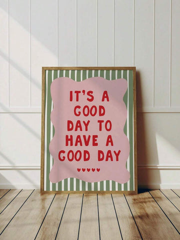 Framed good day quote print leaning against a white paneled wall on a wood floor