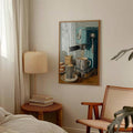 Coffee machine artwork hanging above books and a woven table beside a bedroom chair