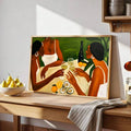 Women sharing drinks artwork leaned on a wood kitchen counter beside pears and striped cloth