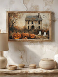 Light wood framed haunted house print with pumpkins and ghosts beside neutral pottery