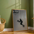 Grayscale basketball dunk silhouette art in a wood frame against a sunlit green wall