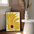 Black-framed yellow sunflower quote print beside a white table and dried grasses