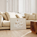 Unframed white pumpkin artwork leaning against a beige sectional in a neutral living room