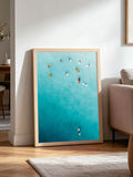 Single teal ocean surf canvas print in a light wood frame beside a modern sofa