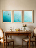 Three vertical ocean wave canvas posters displayed above a warm wood dining table