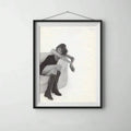 Black-framed matted fashion print of a seated woman wearing dark boots on a light-gray wall