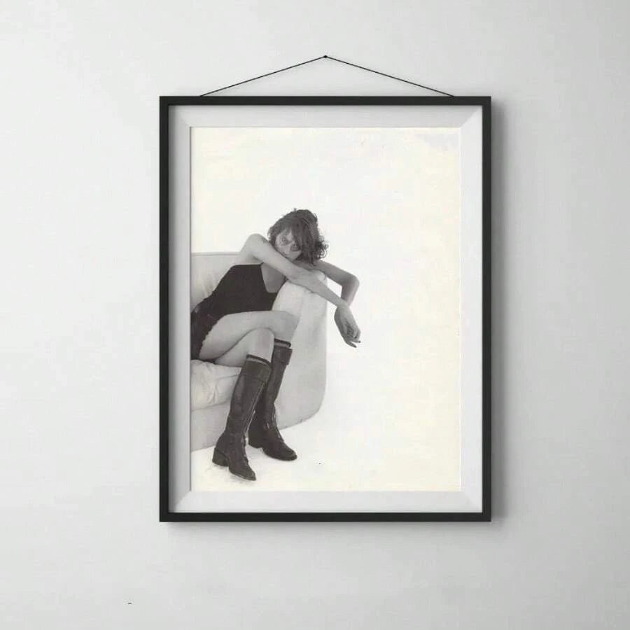 Black-framed matted fashion print of a seated woman wearing dark boots on a light-gray wall
