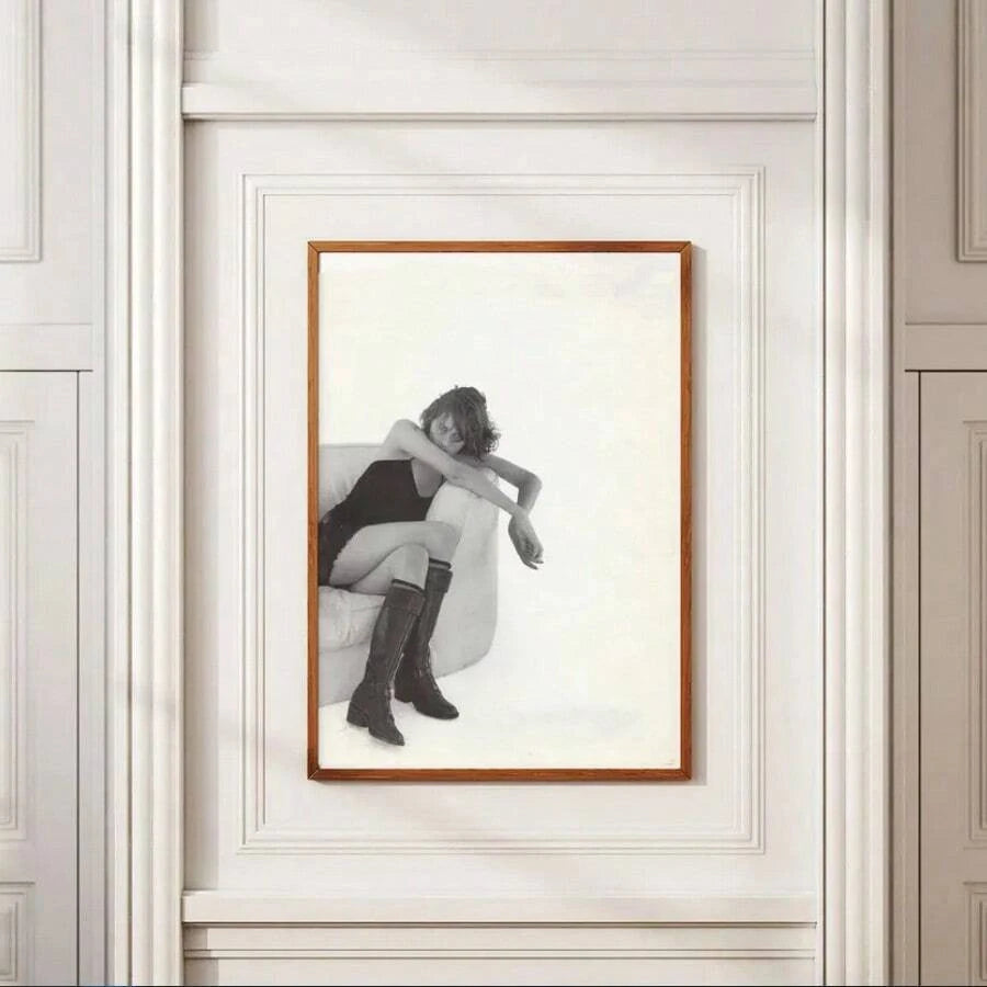 Black-and-white fashion portrait of a woman in knee-high boots seated in an armchair, framed against a white paneled wall