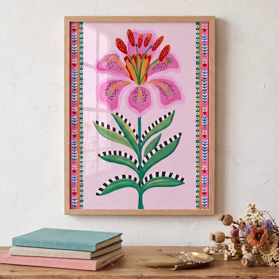 Framed pink lily folk-art print above a wood console with books and dried flowers