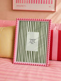 Olive green striped canvas poster in a decorative pink frame on a colorful bedroom bed