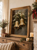 Framed golden bell holiday wall art styled on a rustic wood console with candles and evergreen branches