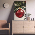 Single red bauble canvas displayed on a pale cabinet beside a chair and plant