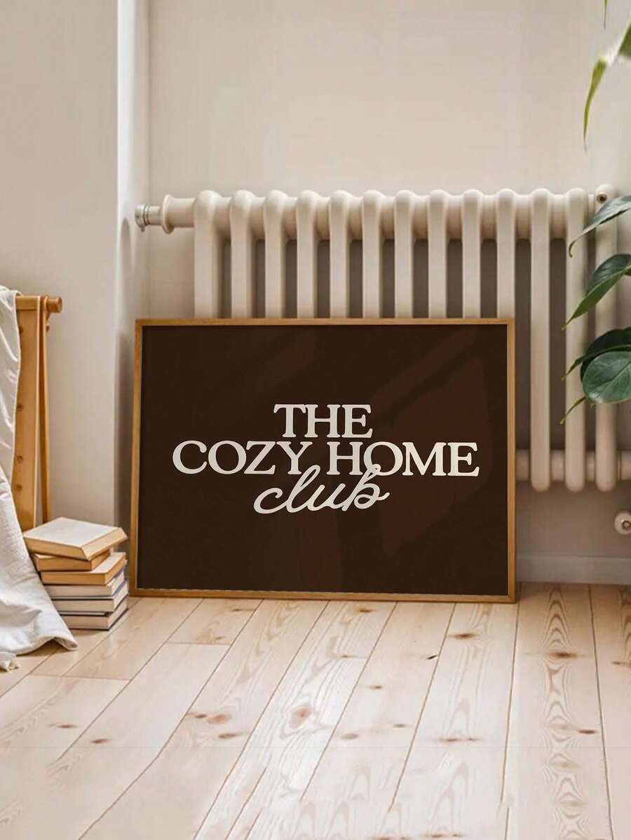 Dark brown Cozy Home Club canvas poster leaned beside books and a plant