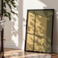 Black-framed botanical window shadow artwork leaning on a sunlit floor against a beige wall