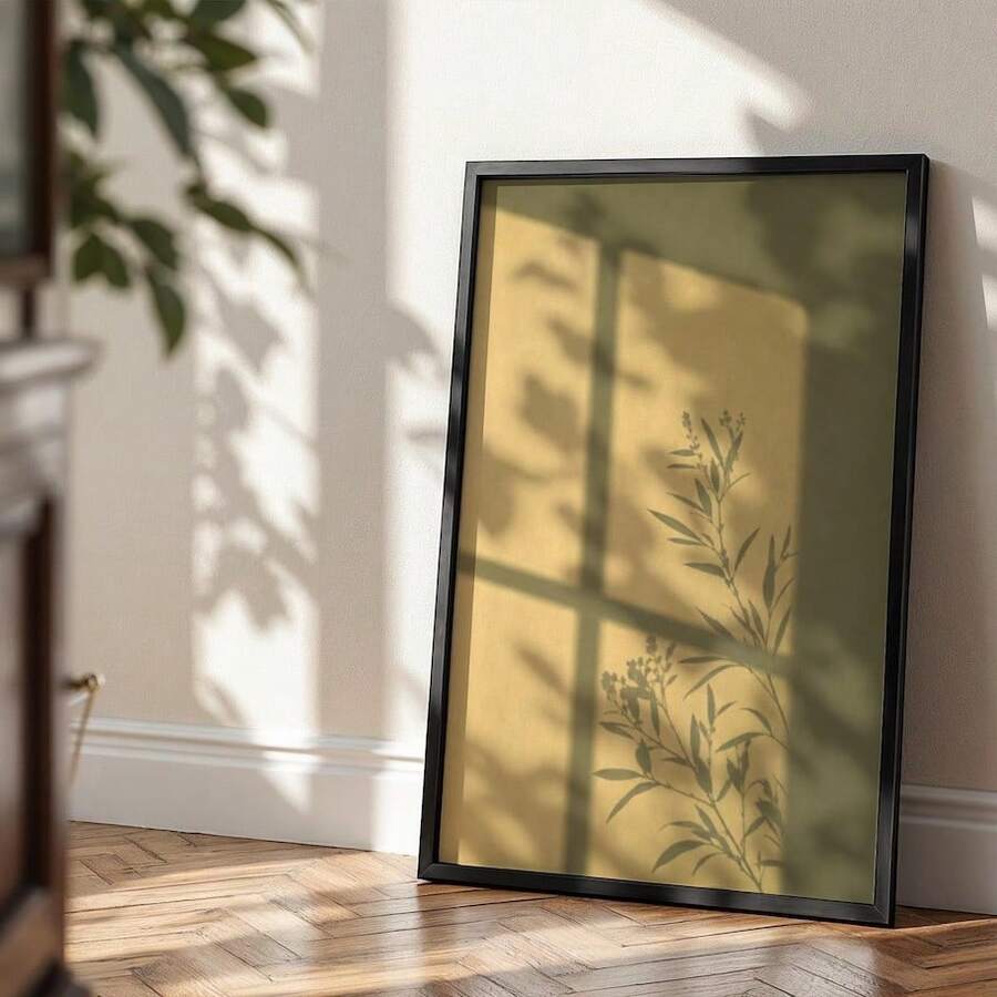 Black-framed botanical window shadow artwork leaning on a sunlit floor against a beige wall