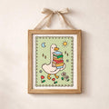 Light wood ribbon-hung frame with white goose carrying colorful books on a sage-green panel