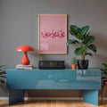 Pink heart dice wall art in a light wood frame above a teal console