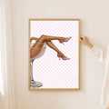 Gold-framed pink cocktail fashion print hung beside sheer curtains and a posed hand
