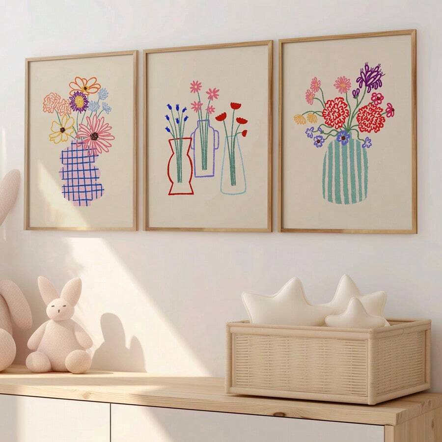 Three colorful hand-drawn floral vase canvases in pale wood frames above a white sofa