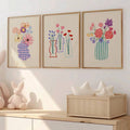 Floral vase canvas trio displayed over a nursery dresser with soft toys and neutral decor