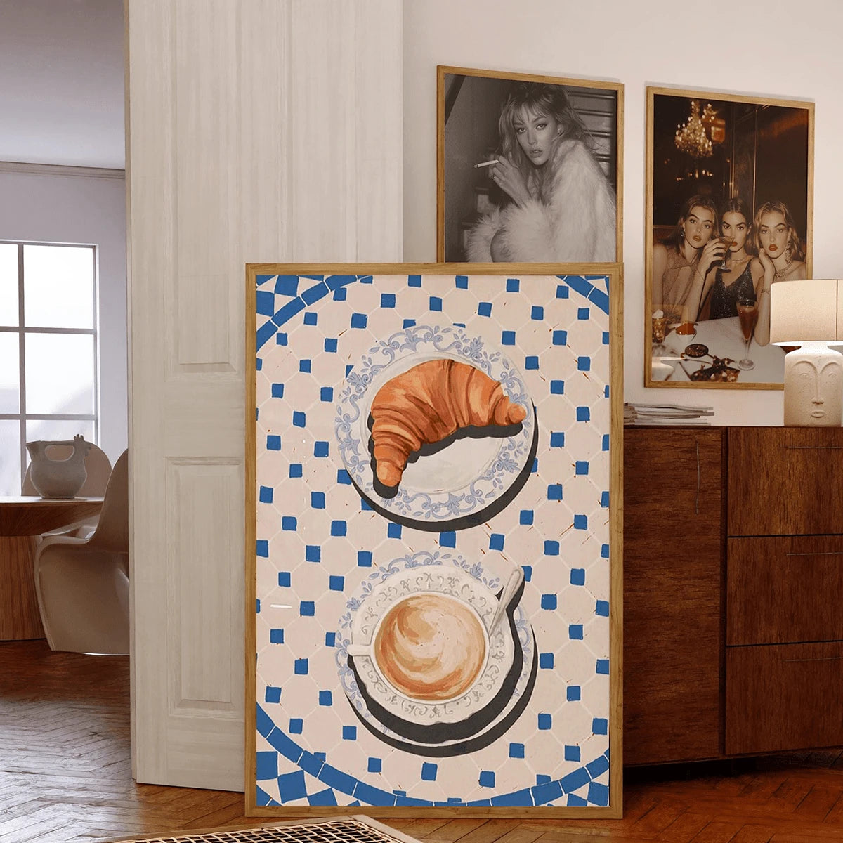 Framed croissant and coffee print displayed by a sunny window and potted plant