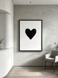 Black heart poster shown on a pale wall beside a modern lounge chair