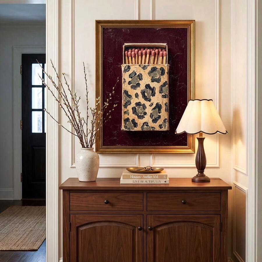 Burgundy matchbox canvas poster in a gold-toned frame above a walnut sideboard with warm lamp light