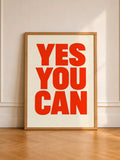 Wood-framed red YES YOU CAN typography print standing against a pale wall