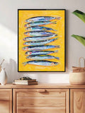 Silver-blue sardine painting on a yellow ground in a black frame over a wood cabinet