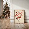 Santa cocktail canvas poster framed beside a Christmas tree and holiday gifts