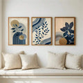 Framed navy leaf artwork arranged above a neutral bench with cream pillows in a bright room