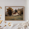 Framed cottage landscape print above a console with candles and books