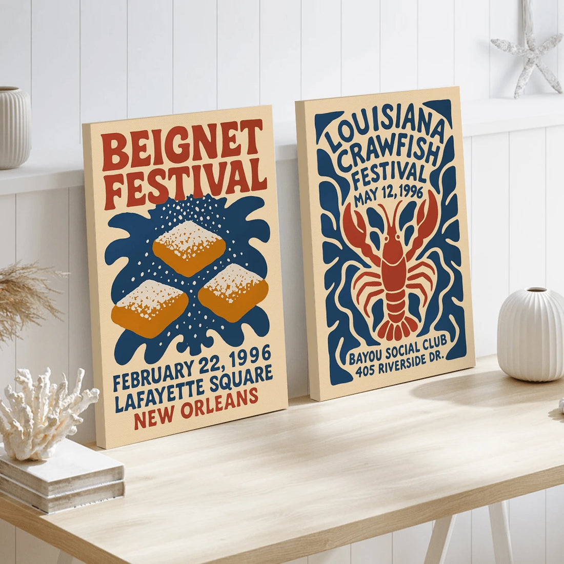 Two vintage-style Louisiana festival posters on a cream console: beignets and a red crawfish in navy and brick red