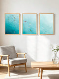 Three teal and aqua surf canvas prints in light wood frames on a Scandinavian living room wall
