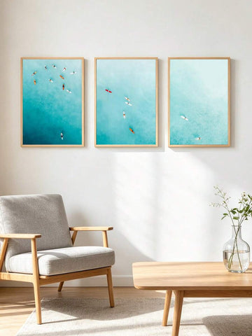 Three teal and aqua surf canvas prints in light wood frames on a Scandinavian living room wall