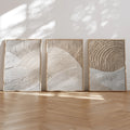 Three framed neutral textured abstract canvas panels with sweeping ivory relief shapes