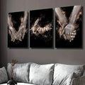 Three black and gold love prints with reaching hands and script above a sofa