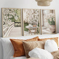 Three light wood-look botanical prints leaning behind a neutral sofa with rust cushions
