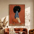 Framed fashion artwork of a Black woman with curls, blue shirt, and orange handbag above a brown sofa