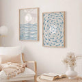 Framed coastal wall art set with blue wave print and blue fish swirl print above white chair