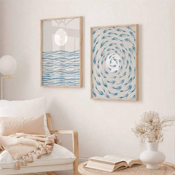 Framed coastal wall art set with blue wave print and blue fish swirl print above white chair