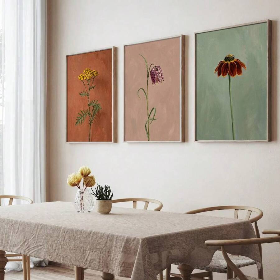 Three framed botanical flower prints above dining table with natural wood chairs