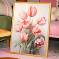 Pink tulip canvas poster in a light wood frame beside a colorful sofa