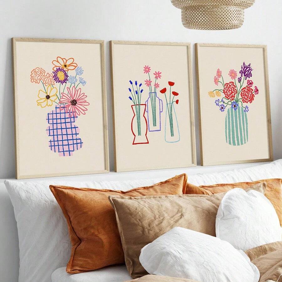 Three colorful hand-drawn floral vase canvases in pale wood frames above a white sofa