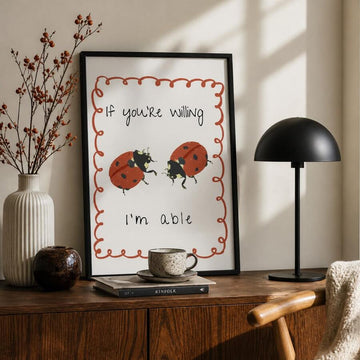 Black-framed ladybug canvas poster with rust scalloped border above a wood sideboard
