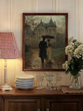 Framed romantic painting of couple walking under umbrella beside manor, styled above buffet with lamp and flowers