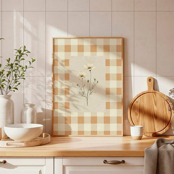Framed daisy botanical print with a cream and tan gingham border on a sunlit kitchen counter